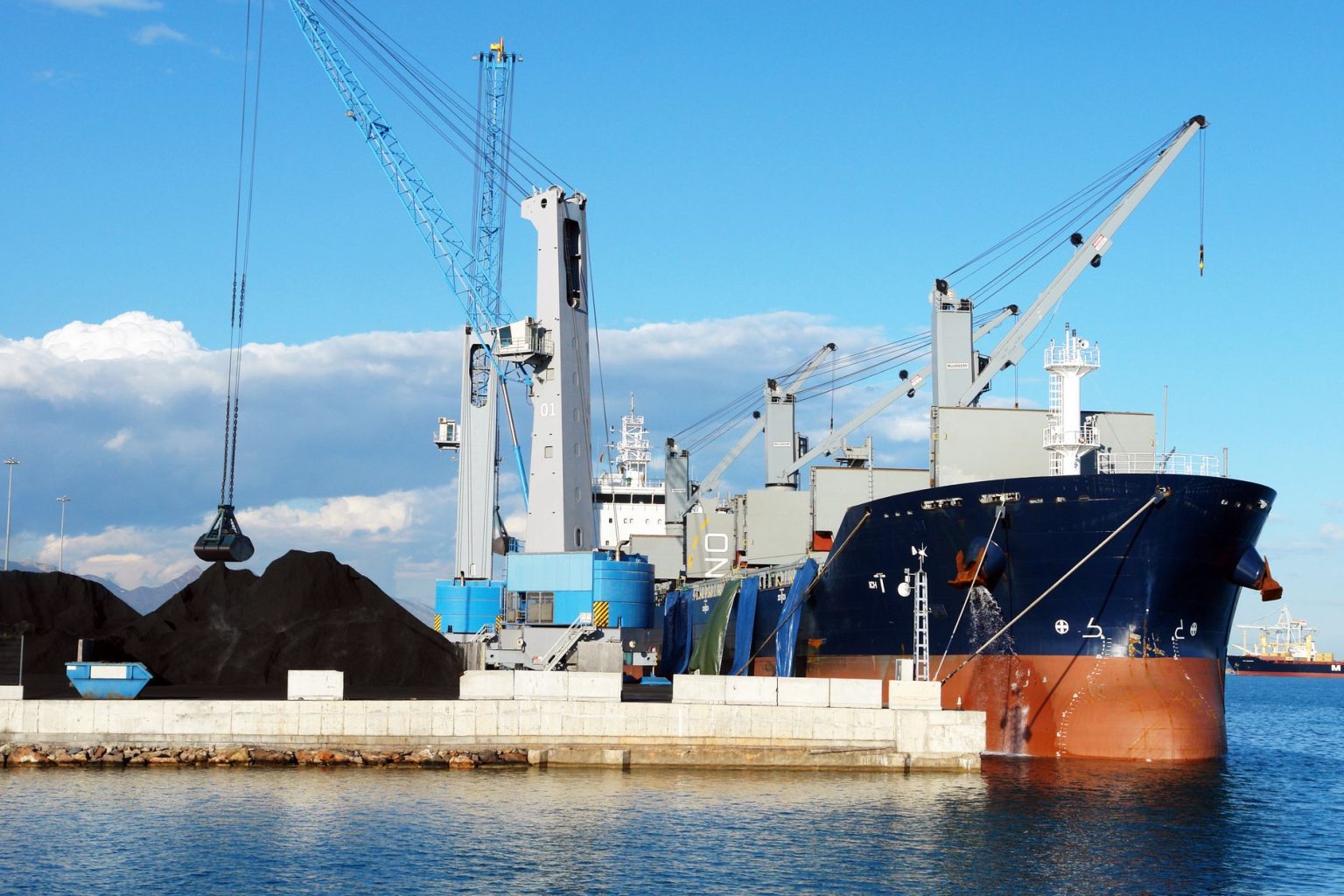Navio cargueiro com guindastes em um porto industrial durante o carregamento de minerais.