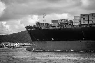 Navio porta-contêineres atracado no Porto de Santos, com estruturas portuárias ao redor.