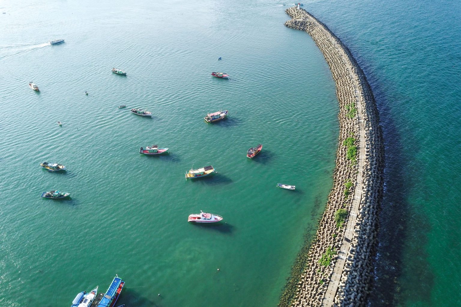 Vista aérea de um longo quebra-mar em construção no mar, com embarcações ao redor.
