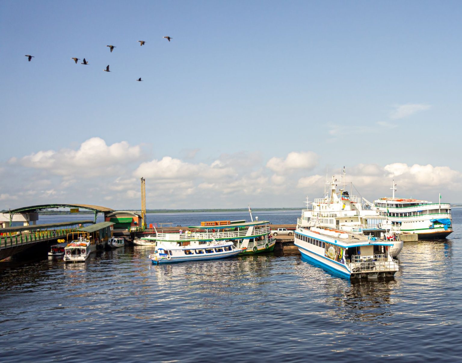 Embarcações atracadas em um porto movimentado de Manaus, às margens de um rio, sob céu azul.