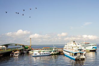Embarcações atracadas em um porto movimentado de Manaus, às margens de um rio, sob céu azul.