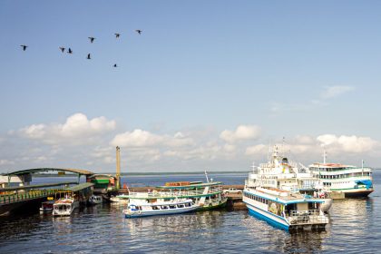 Embarcações atracadas em um porto movimentado de Manaus, às margens de um rio, sob céu azul.