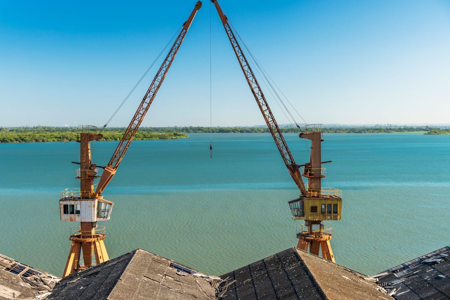 Dois guindastes portuários posicionados sobre uma área fluvial no Rio Grande do Sul.