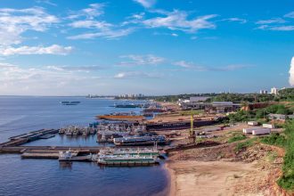 Vista aérea de um porto às margens do Rio Negro, em Manaus, com embarcações atracadas e a cidade ao fundo.