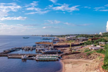 Vista aérea de um porto às margens do Rio Negro, em Manaus, com embarcações atracadas e a cidade ao fundo.
