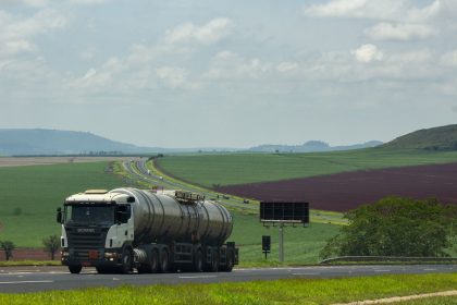 Caminhão de carga trafega por uma rodovia entre extensos campos agrícolas.